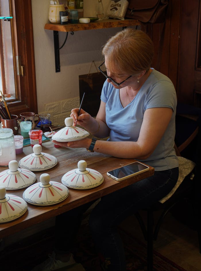 services-01 A skilled artisan hand-paints traditional Turkish pottery in a cozy workshop in Bursa, Türkiye.