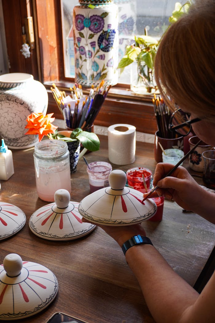 services-02 An artist carefully paints intricate designs on Turkish pottery in a sunlit studio in Bursa, Türkiye.