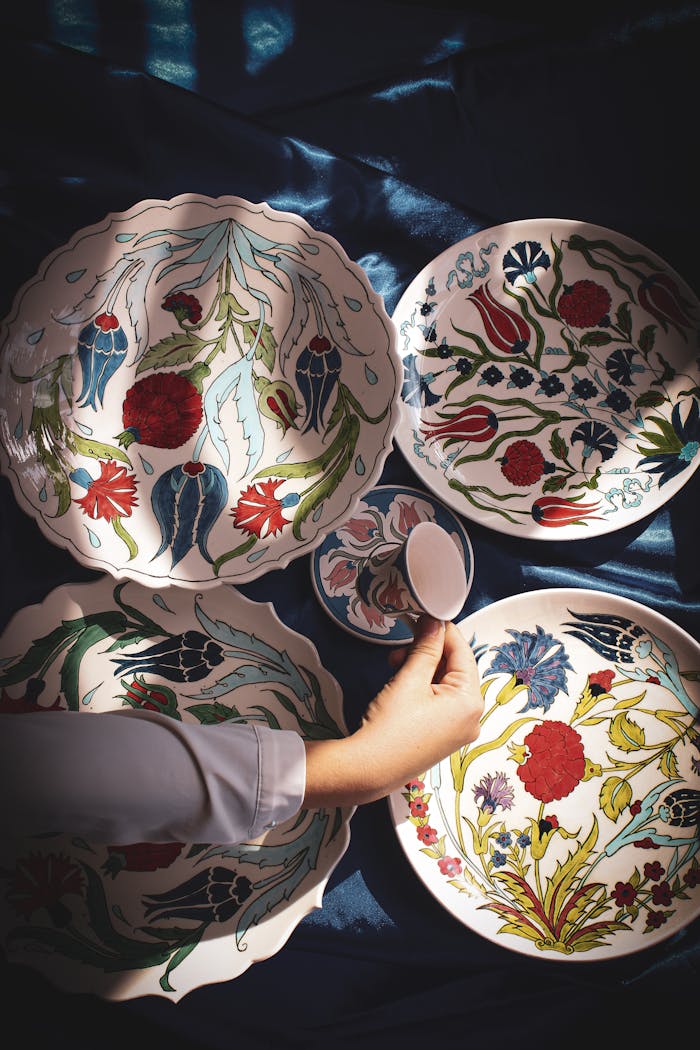 services-04 Hand arranging colorful floral ceramic plates on dark fabric. Perfect for home decor inspiration.
